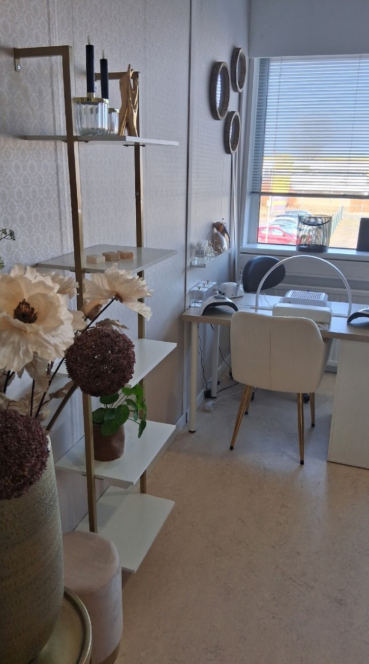 De salon: werktafel met nagellamp, witte stoel en planken met bloemen bij het raam