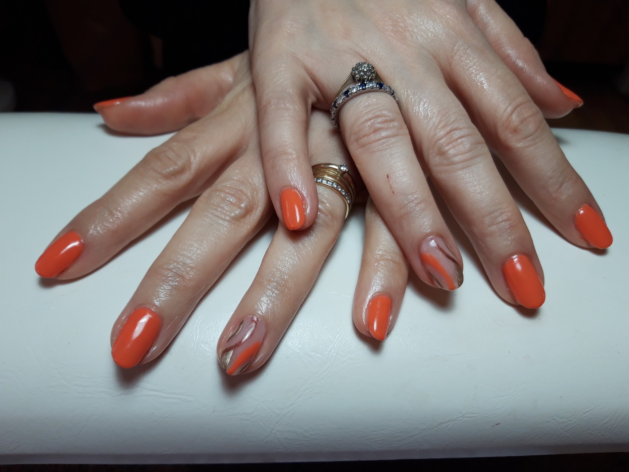 Handen met oranje gellak en gemarmerde accentnagels